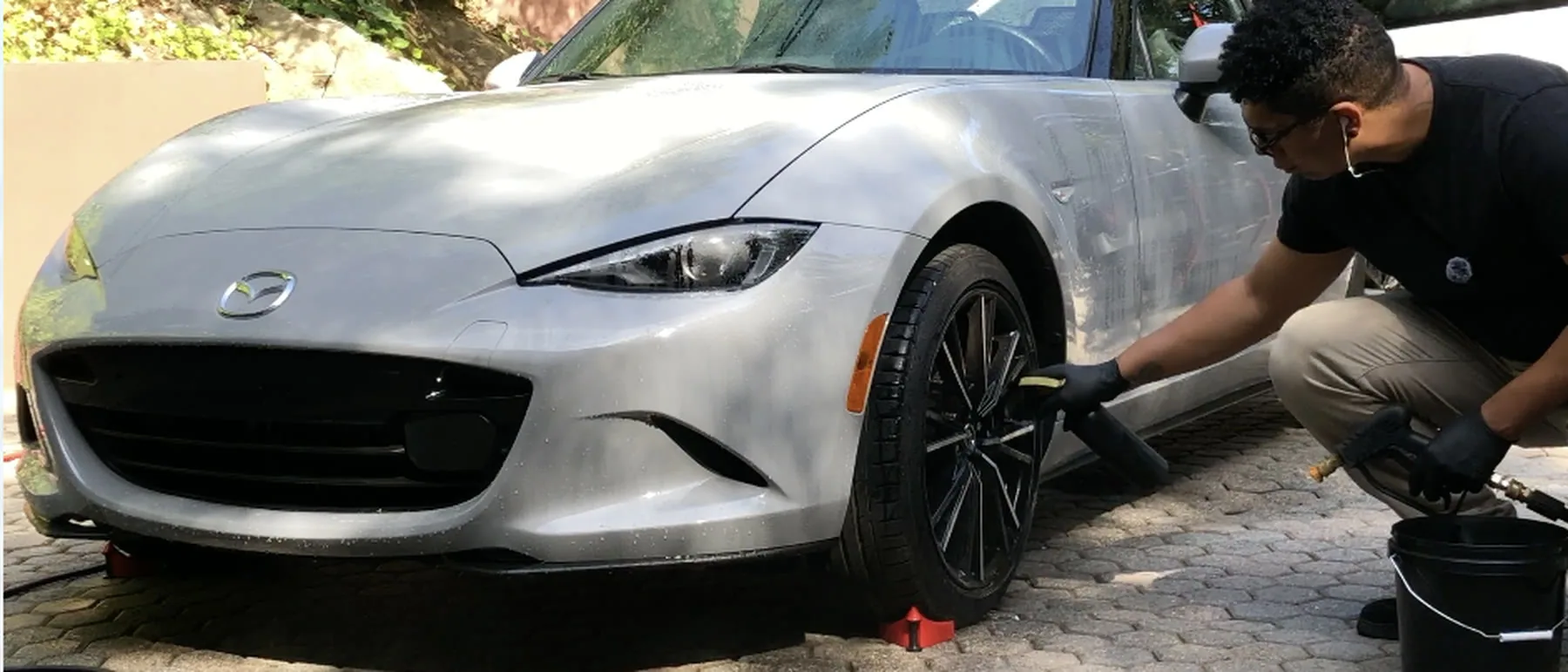 Tyroo West at the front wheel of a silver Mazda MX-5 on a paver driveway, pressure gun in hand