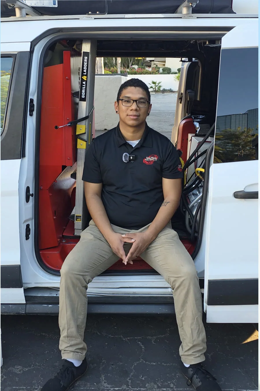 Tyroo West sitting in the open side door of the TailorMade van, the ladder, hose reels and equipment racked up behind him
