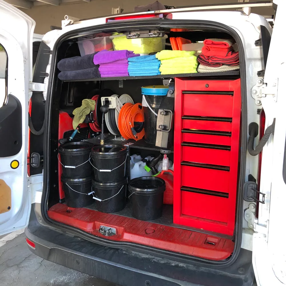 The back of the TailorMade van open at a job, showing folded microfibre towels, hose reels, buckets and the red tool chest
