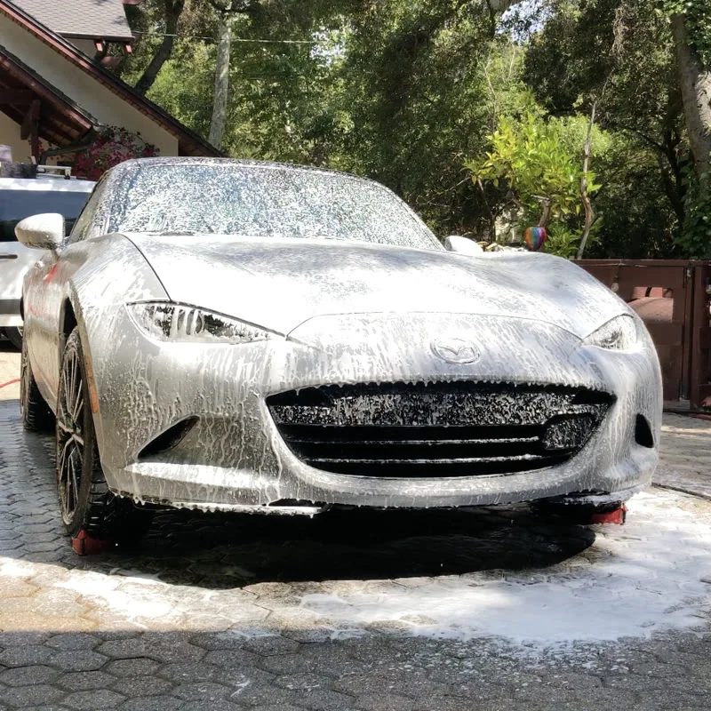 A Mazda MX-5 covered in snow foam during a hand wash on a paver driveway in Westlake Village, CA