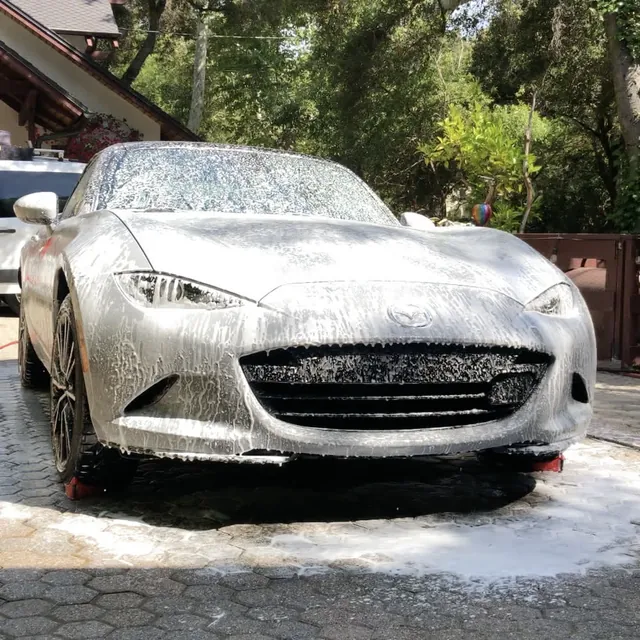 A Mazda MX-5 covered in snow foam on a paver driveway during a hand wash