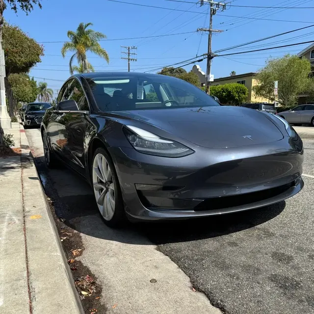 A dark gray Tesla Model 3 parked at the curb, freshly washed and dried