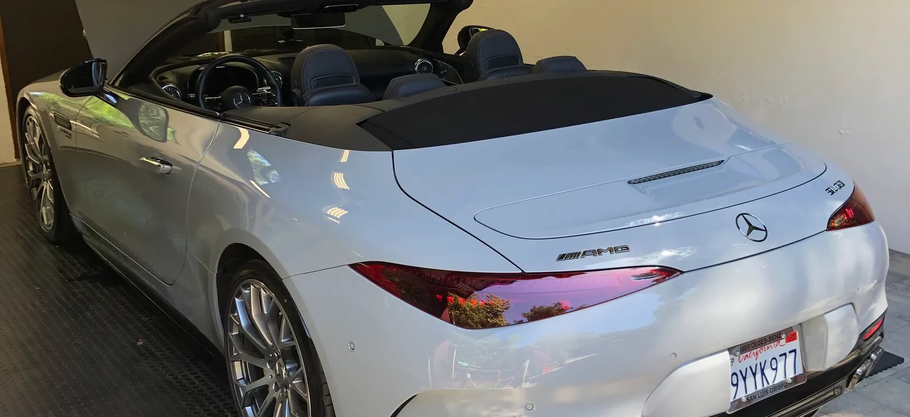 A white Mercedes-AMG SL 63 detailed in a garage, rear three-quarter with the roof down and the paint finished