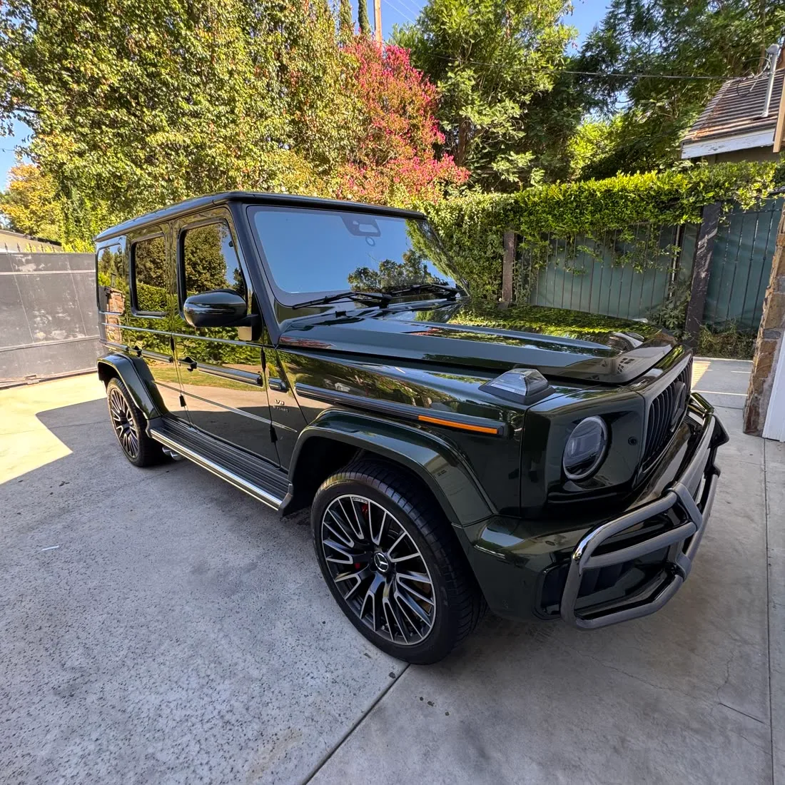 A dark green Mercedes-AMG G-Wagon detailed on a driveway, paint finished and reflecting the trees behind it