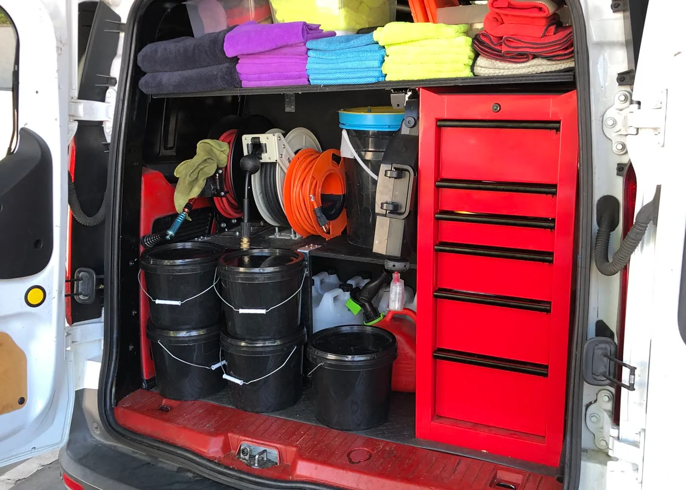 The TailorMade mobile detailing van open, showing folded microfibre towels, hose reels, buckets and the tool chest