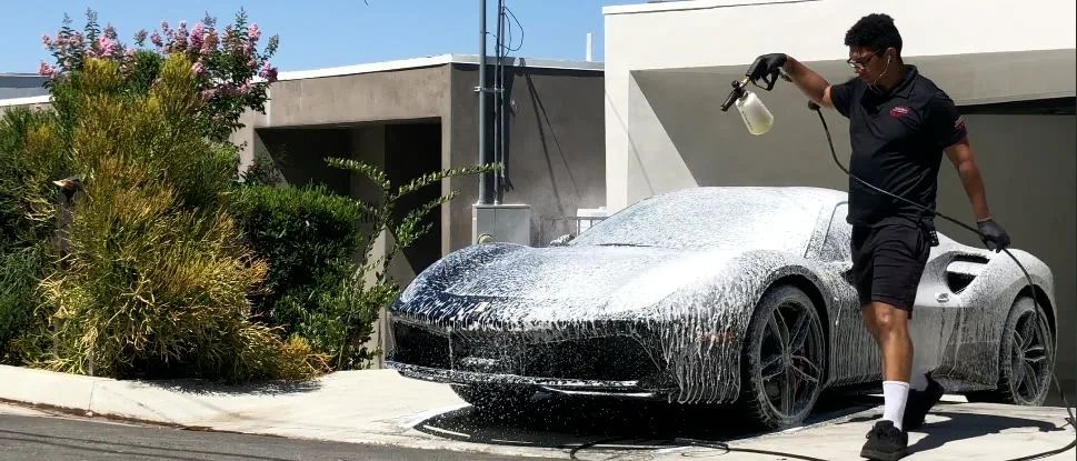 Tyroo West spraying foam across a white Ferrari 488 on a driveway in the San Fernando Valley