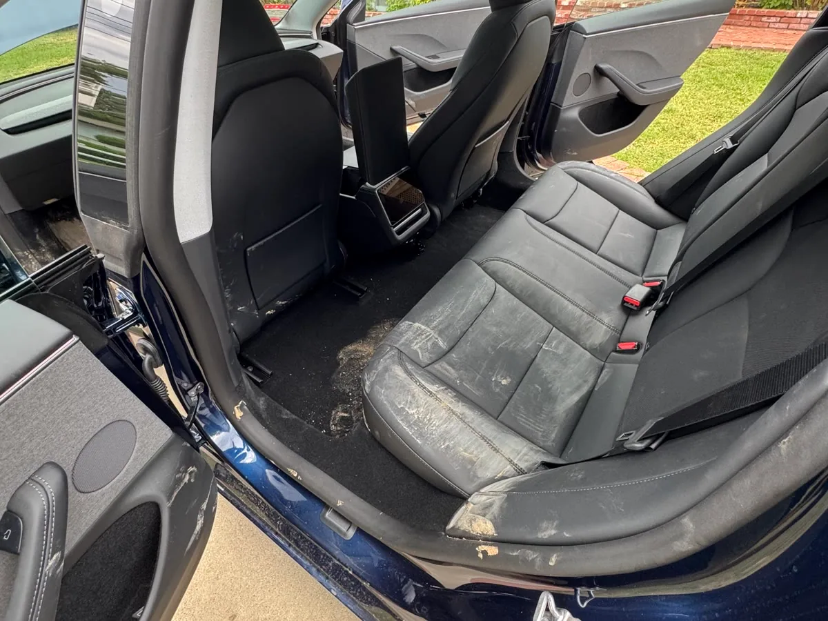 The rear seats of a navy Tesla Model 3 caked in dried mud before an Interior Reset