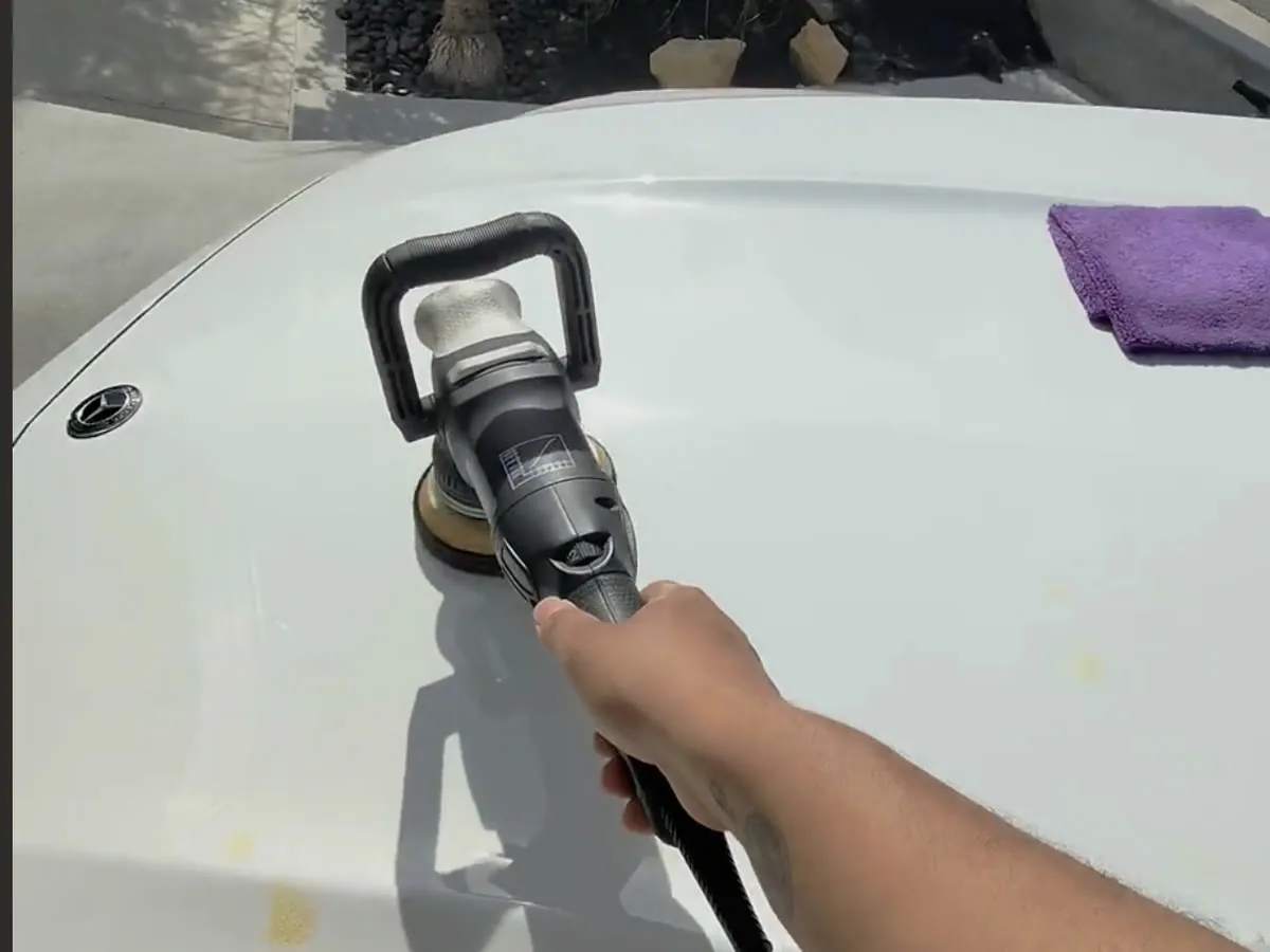 A dual action polisher working the bonnet of a white Mercedes, a folded microfibre towel laid beside it