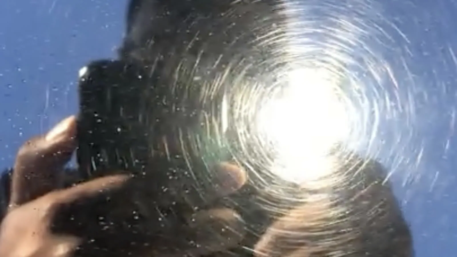 A work light reflected in swirled paint, the beam smeared into a spiral halo of fine scratches