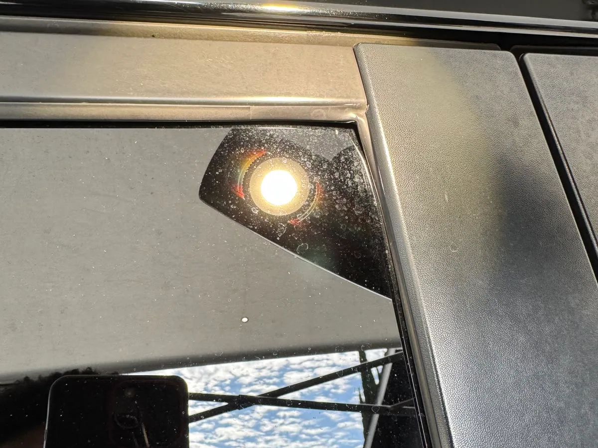 Hard water spotting across a car window with the sun behind it, the kind of mineral deposit that etches glass and paint alike