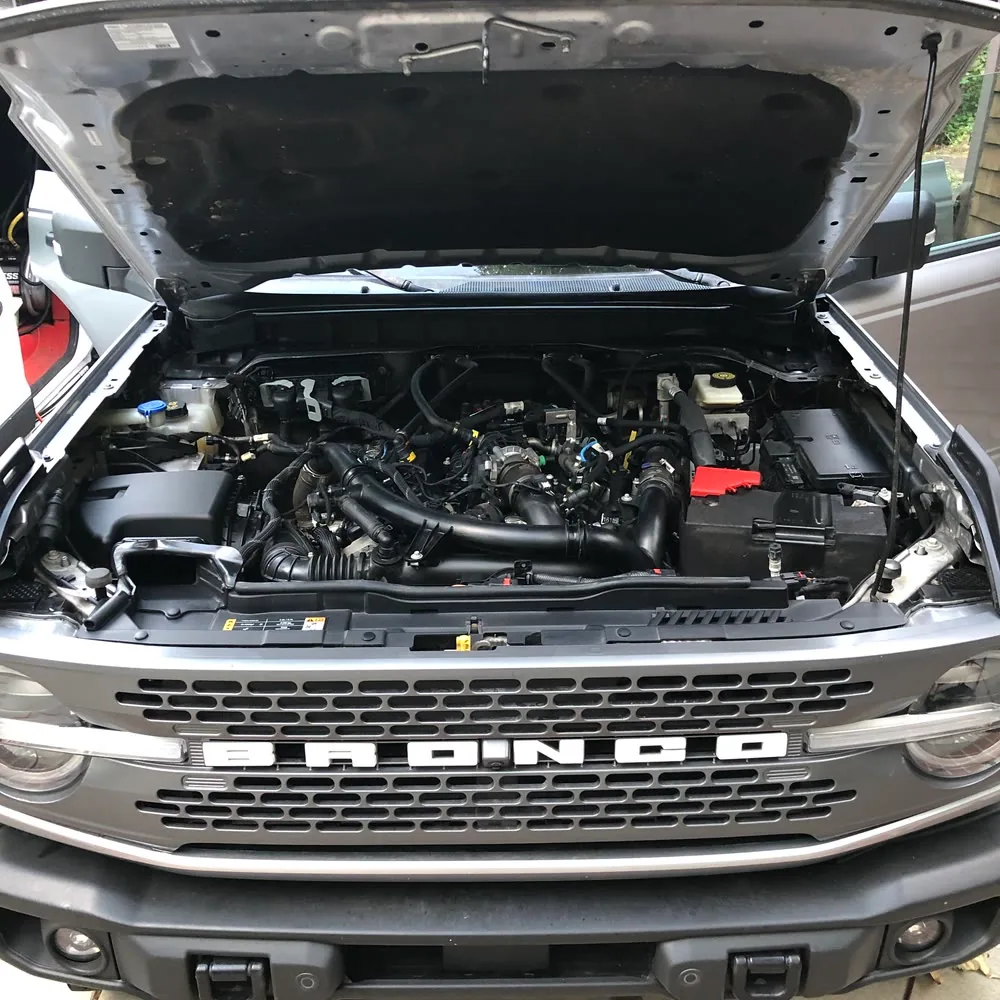 The engine bay of a Ford Bronco cleaned and dressed, hood raised on a driveway