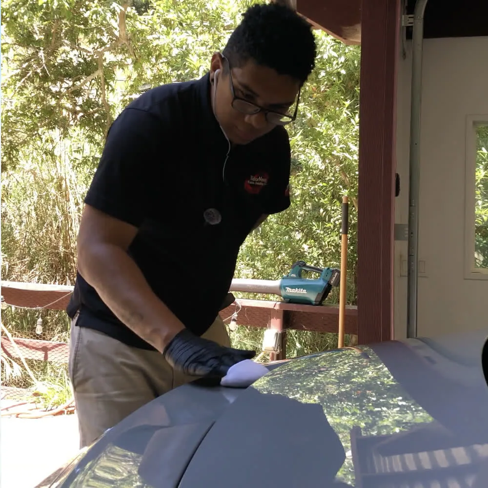 Tyroo West hand-applying a ceramic coating to a dark bonnet with a foam applicator