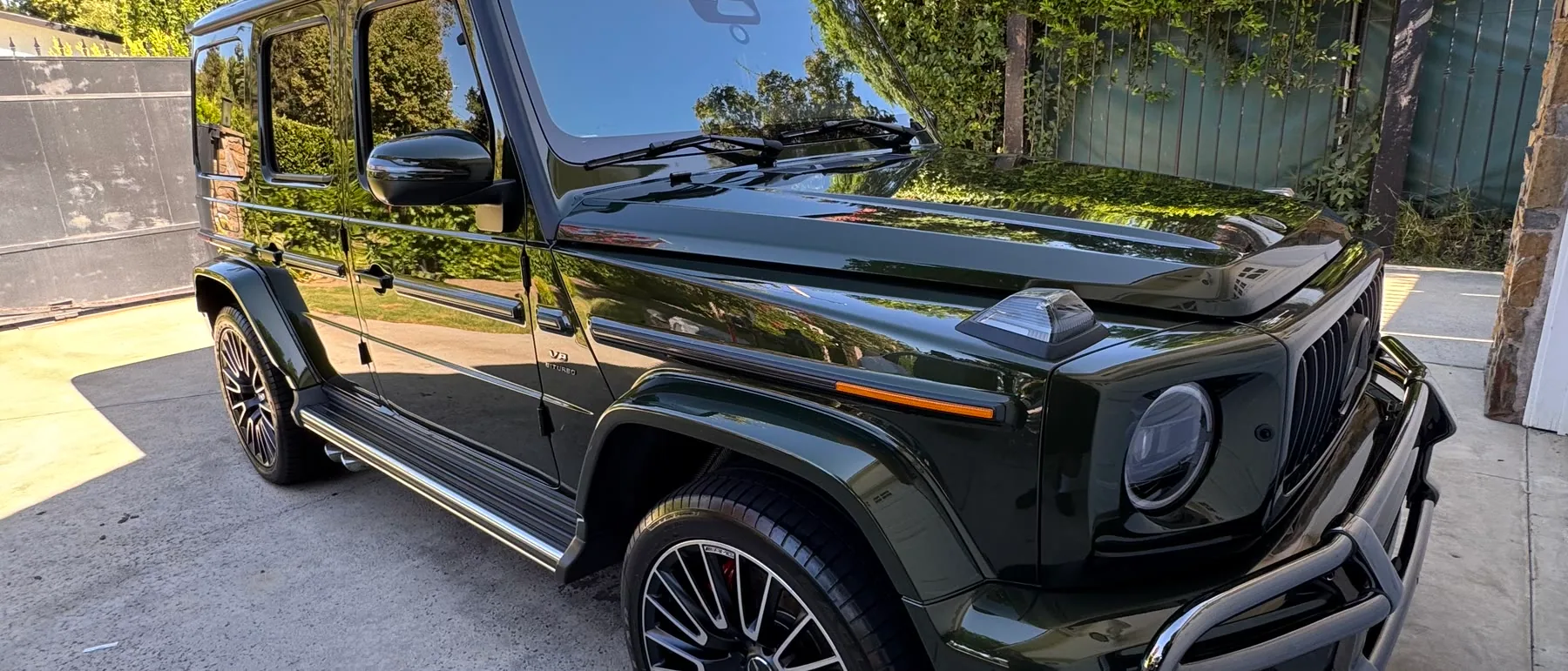 A dark green Mercedes-AMG G-Wagon on a driveway, the trees overhead mirrored in the bonnet