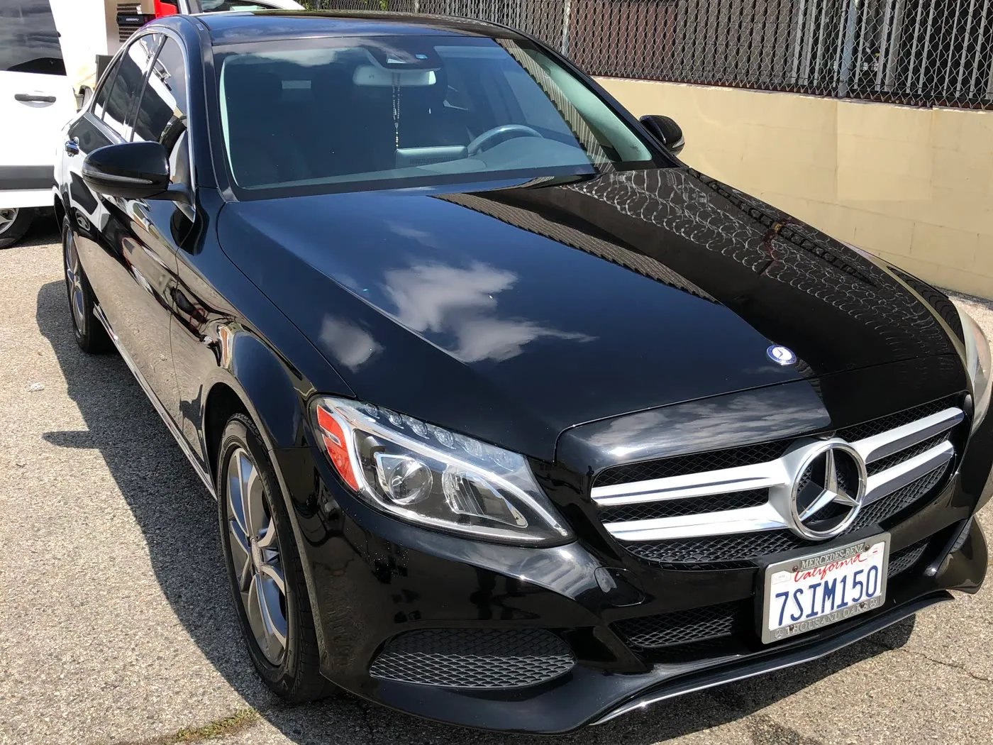 A black Mercedes-Benz C-Class after a luxury detail, holding sharp cloud reflections across the hood