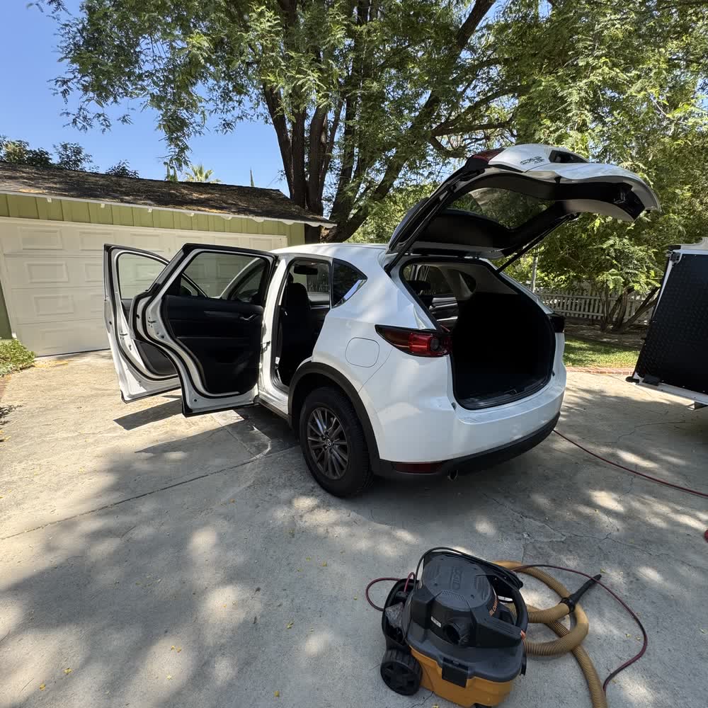 A white Mazda CX-5 mid-detail on a driveway, every door and the tailgate open with the extractor running