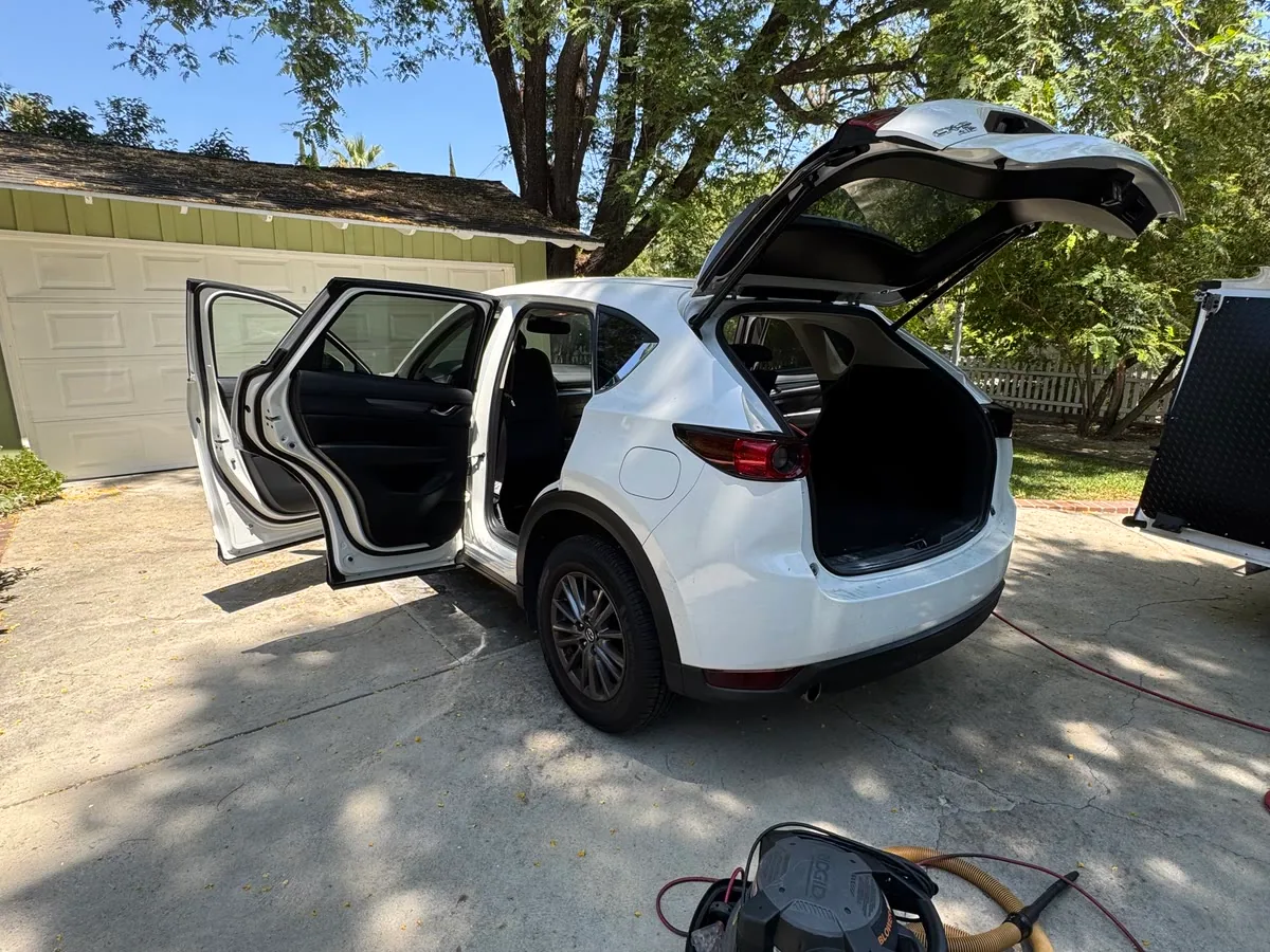 A white Mazda CX-5 on a driveway mid-detail, every door and the tailgate open with the extractor running beside it