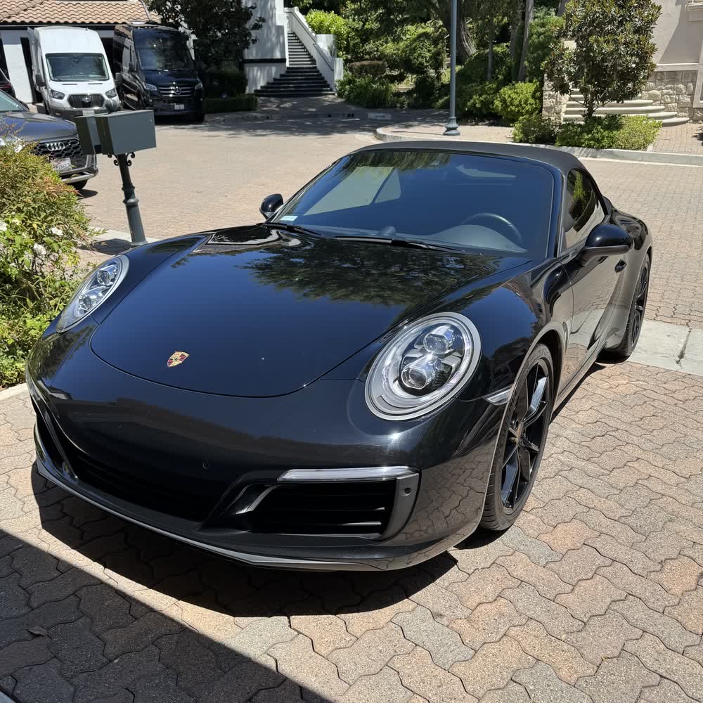 A black Porsche 911 on a paver driveway, paint corrected to a deep even gloss