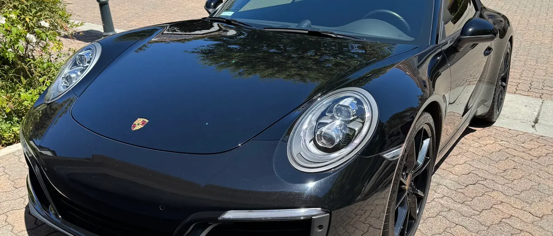 A black Porsche 911 on a paver driveway after paint correction, the finish deep and evenly glossy